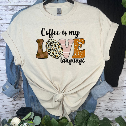 Beige t-shirt with 'Coffee is my love language' text and graphics on a wooden surface.